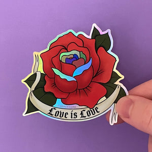 A holographic sticker of a red rose drawn in the traditional American tattoo style with a tattoo banner that says "Love Is Love" in a gothic font. The red rose has Pride-colored petals as accents.