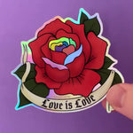 Load and play video in Gallery viewer, A video demonstrates the holographic effect of a sticker of a red rose drawn in the traditional American tattoo style with a tattoo banner that says "Love Is Love" in a gothic font. The red rose has Pride-colored petals as accents.
