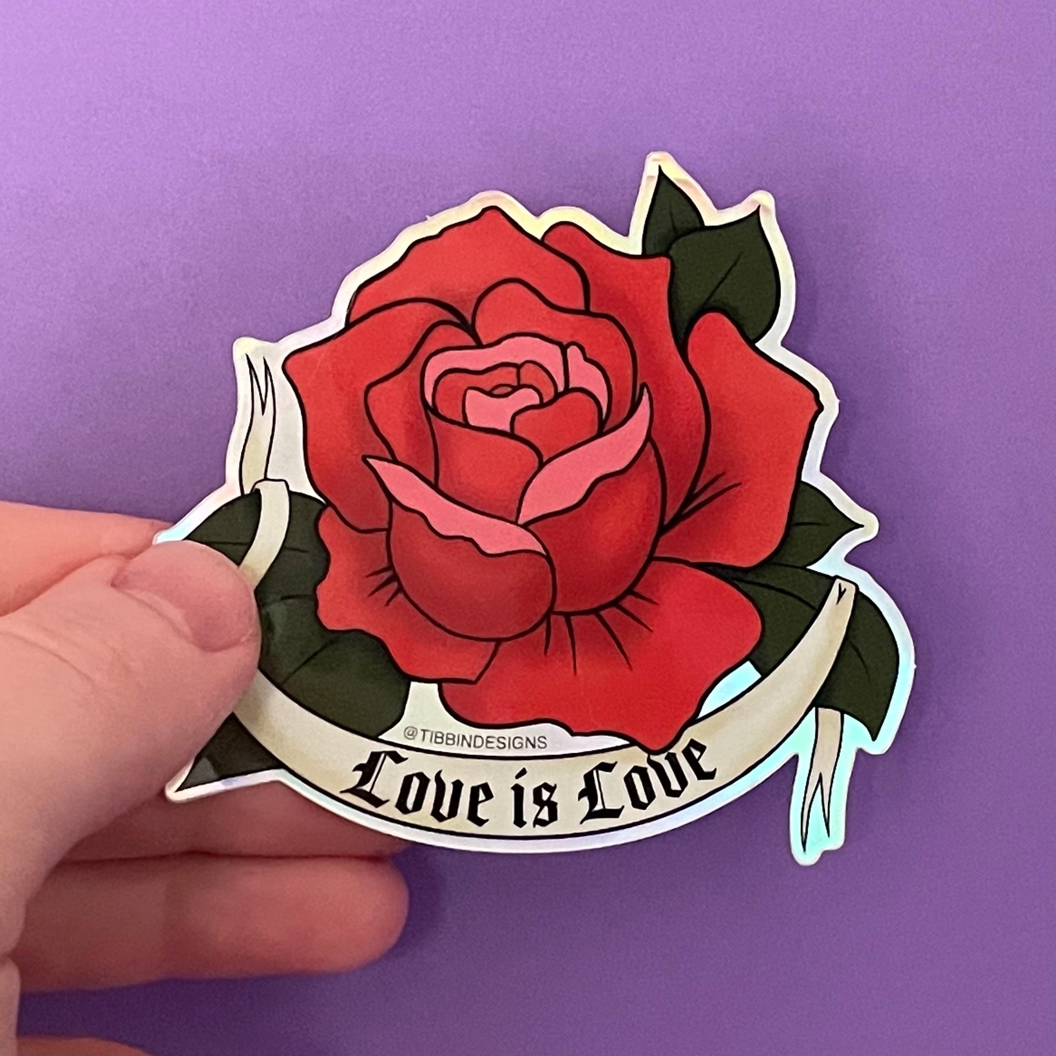 A holographic sticker of a red rose drawn in the traditional American tattoo style with a tattoo banner that says &quot;Love Is Love&quot; in a gothic font. The red rose has pink petals as accents.