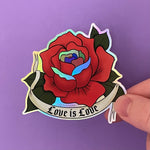 Load image into Gallery viewer, A holographic sticker of a red rose drawn in the traditional American tattoo style with a tattoo banner that says "Love Is Love" in a gothic font. The red rose has Pride-colored petals as accents.

