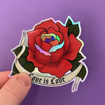 Load image into Gallery viewer, A holographic sticker of a red rose drawn in the traditional American tattoo style with a tattoo banner that says "Love Is Love" in a gothic font. The red rose has Pride-colored petals as accents.
